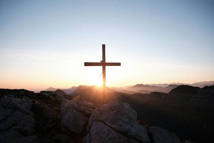 Wooden cross on rocky mountain at sunrise, representing RaptureTok and end of the world prediction discussions.