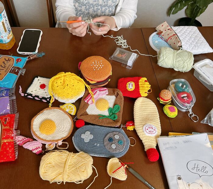 Japanese fiber artist crocheting realistic food-inspired accessories like fries, burgers, and eggs on a wooden table.