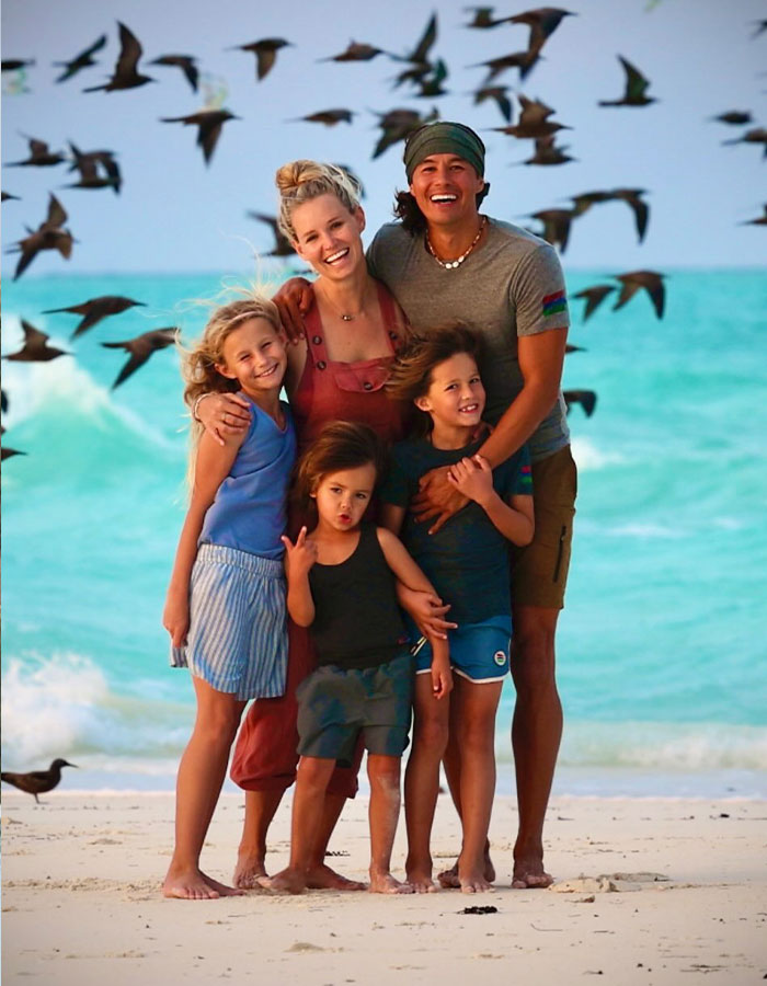 Family posing on beach with ocean waves and birds flying as dad linked arms with kids in casual summer clothes. Family posing on beach with ocean waves and birds flying as dad linked arms with kids in casual summer clothes.