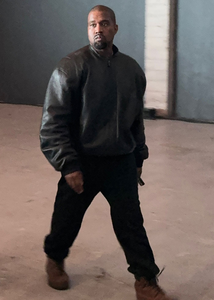 Kanye West walking in a dark jacket and pants, sparking controversy over public listing of daughter North in betrayal list.