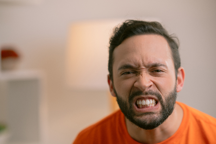Angry man with beard in an orange shirt expressing frustration, related to husband calls pregnant wife and baby issues.