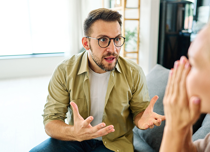 Man with glasses arguing intensely with partner during breakup after long relationship in a modern living room.