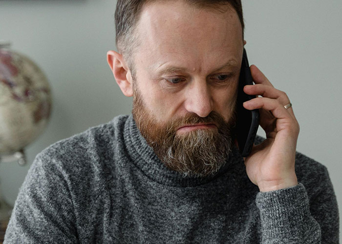 Man with a beard wearing a gray sweater talking on the phone, reflecting on incredible coincidences that sound fake but are true.