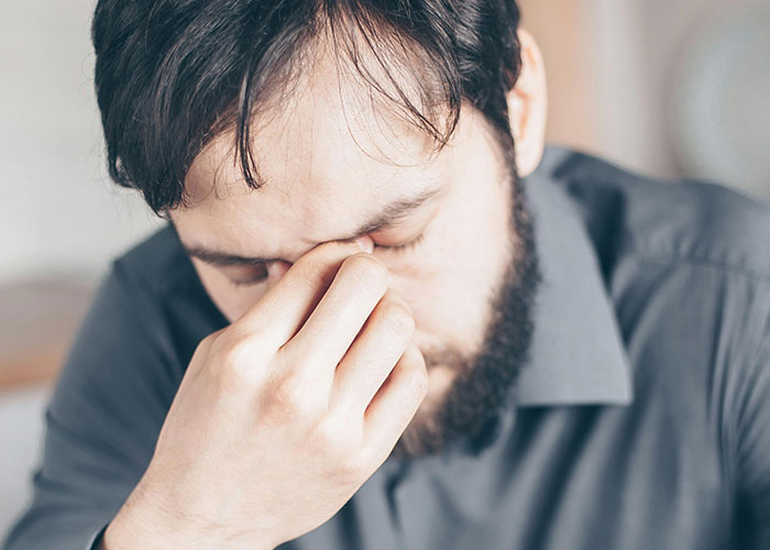 Man with beard in gray shirt rubbing eyes, appearing frustrated and overwhelmed by criminal fails situation.