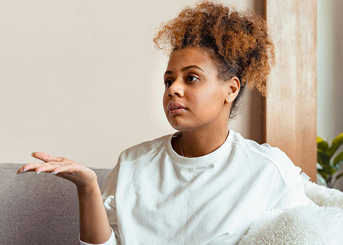 Woman with curly hair sitting on a couch, gesturing with hand, reflecting on the creepiest things women do that cross the line.