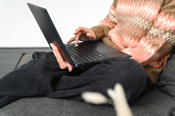 Person in a patterned sweater using a laptop on a couch, illustrating the inclusion of AI into everyday activities.