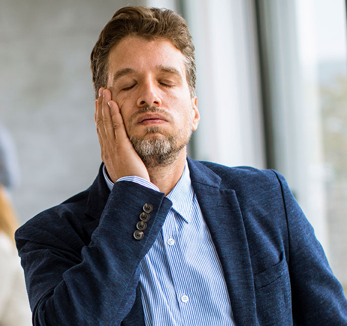 Man in a business suit with eyes closed, resting face on hand, reflecting on the inclusion of AI in modern trends.