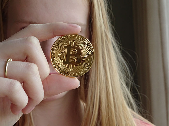 Person holding a golden Bitcoin coin close to their face, symbolizing inclusion of AI into everything.