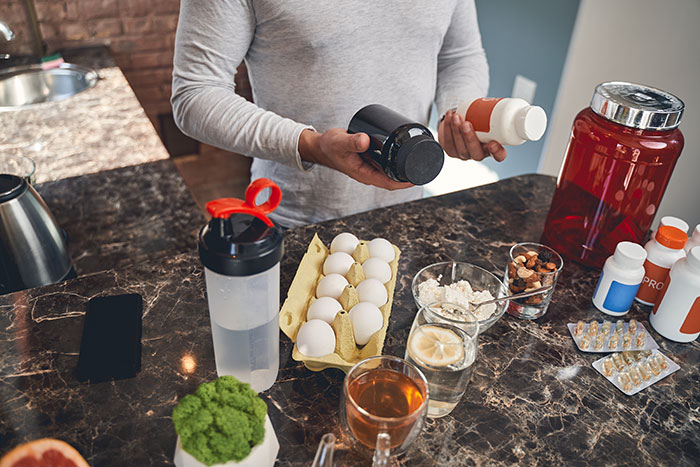 Person holding supplement bottles with various vitamins, eggs, and healthy foods on kitchen counter, highlighting AI inclusion.