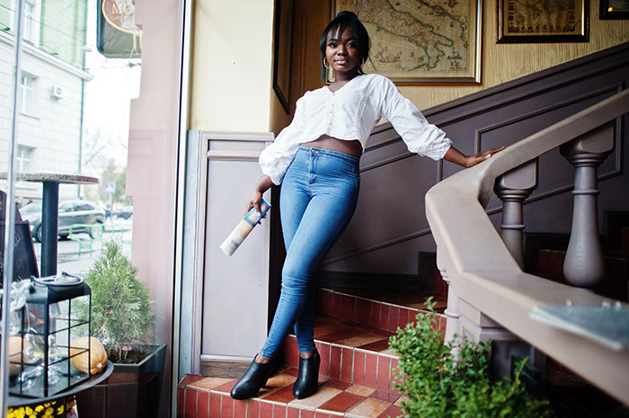 Young woman leaning on staircase railing inside a cafe, holding a paint roller, symbolizing inclusion of AI into everything.