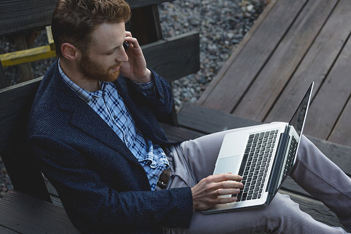 Man using laptop outdoors on wooden bench, representing the inclusion of AI into modern technology trends.