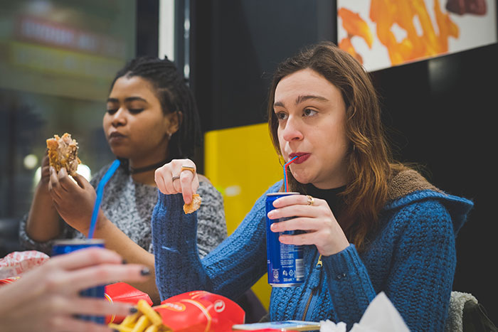 Two women eating fast food and drinking soda, highlighting the inclusion of AI into everyday activities and trends.