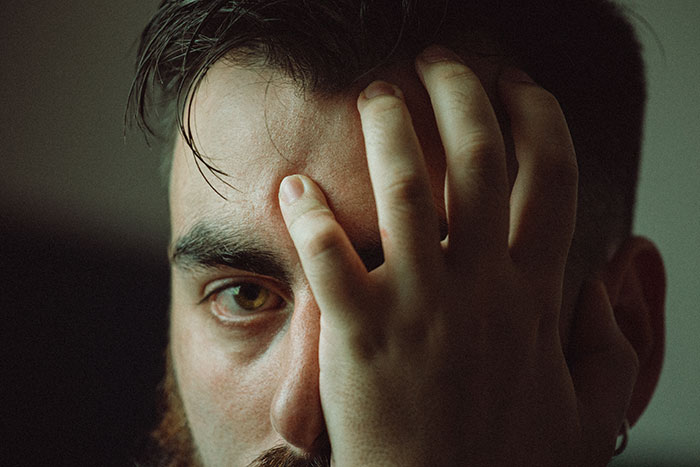 Man with beard covering half of his face with hand, reflecting on the inclusion of AI into everything in modern trends.