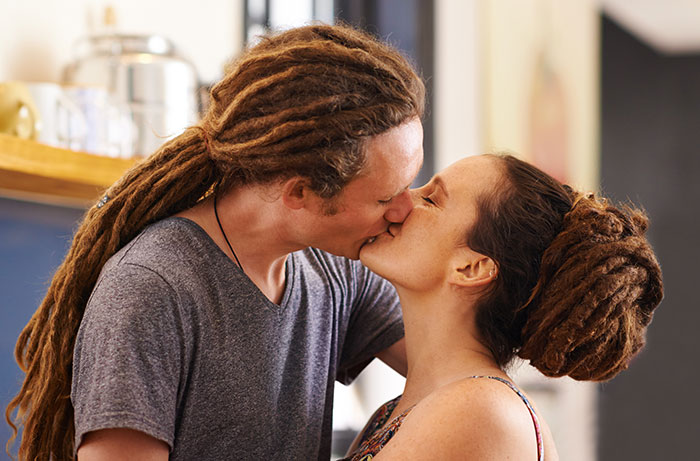 Couple with dreadlocks sharing a kiss indoors, illustrating human connection amidst inclusion of AI into everything trends.