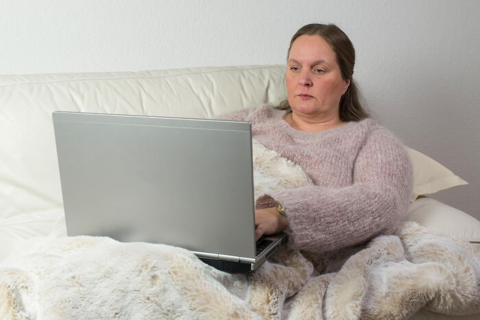 Woman sitting on a couch using a laptop, discovering secret stories of partners and spouses while surfing online.