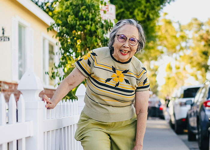 Elderly woman smiling by a white fence outside her new home, enjoying hidden gems discovered after moving in.