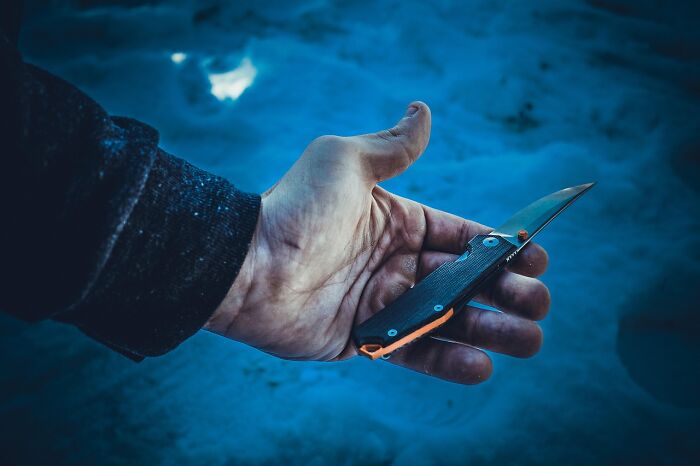 Hand holding a folding knife outdoors, illustrating chaotic stories shared by food delivery drivers.