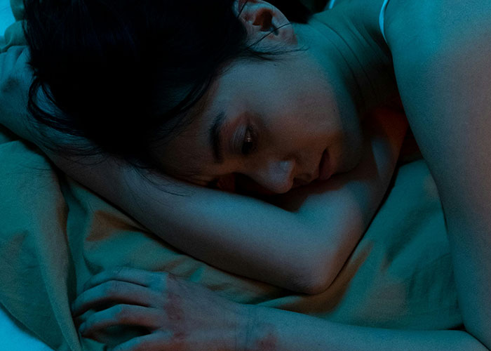 Person lying awake in bed at night, looking distressed and fearful, illustrating terrifying true stories.