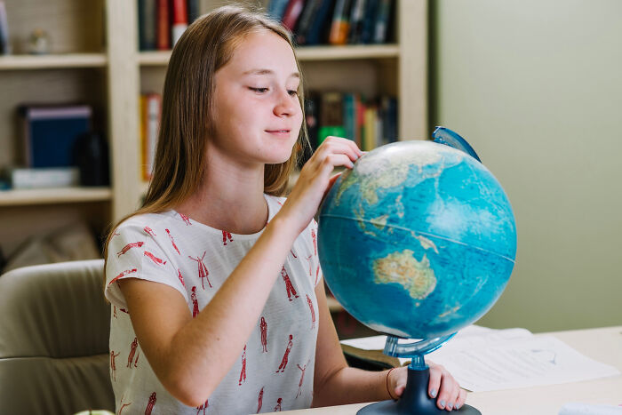 Girl spinning a globe while sitting at a desk, illustrating a mind-boggling conversation about adults and survival skills.