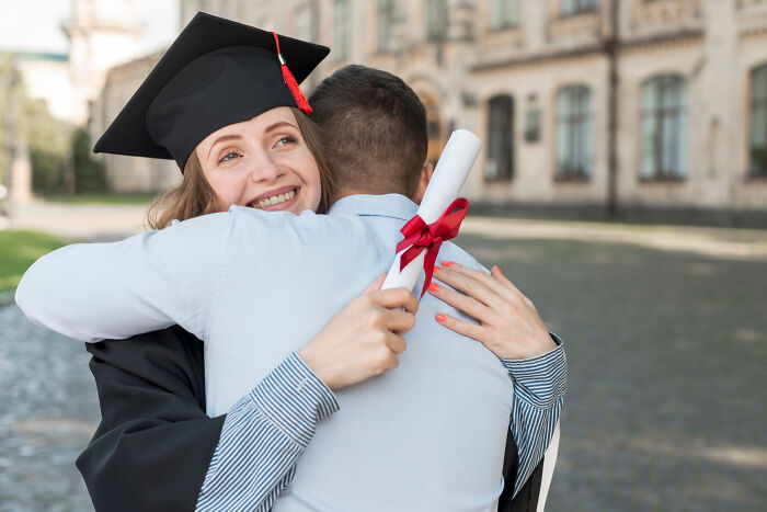 Young woman in graduation cap hugging a man while holding a diploma, expressing joy and gratitude with life-changing sentences.