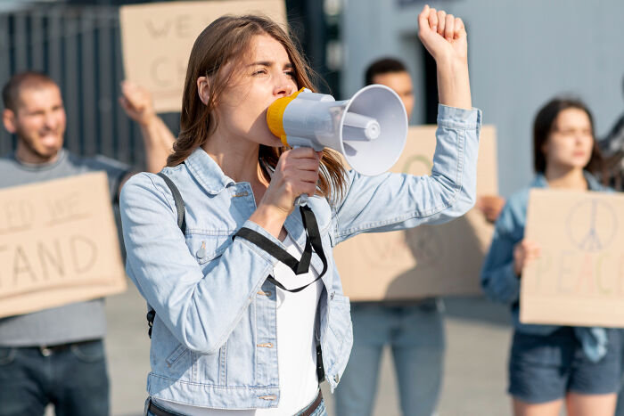 Young woman leading a protest with a megaphone, symbolizing real-life stories of people becoming what they once hated.