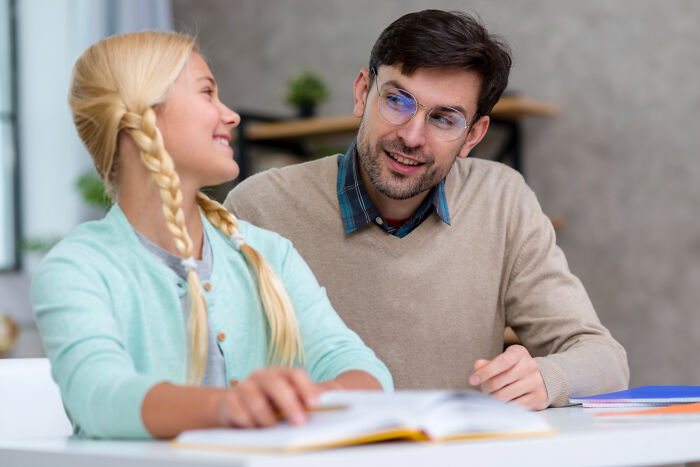 Teacher wearing glasses talking to a smiling female student with braids during a study session at school.