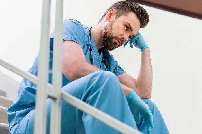 Young man in medical scrubs sitting on stairs, deep in thought, reflecting on life-changing sentences tattooed on hearts.