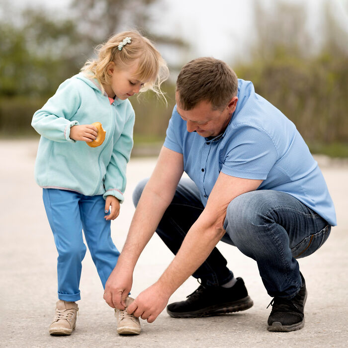 Man crouching to help little girl tie shoes outdoors, representing the theme of shocking family secrets uncovered.