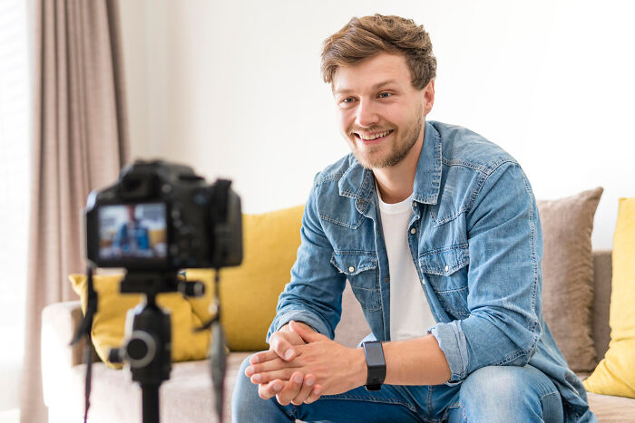 A smiling young man in a denim jacket recording a video about relationship dealbreakers in a cozy living room.