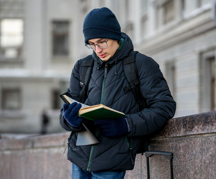 Student reading a book outdoors in winterwear, illustrating shocking school incidents involving hypnosis and secret affairs.
