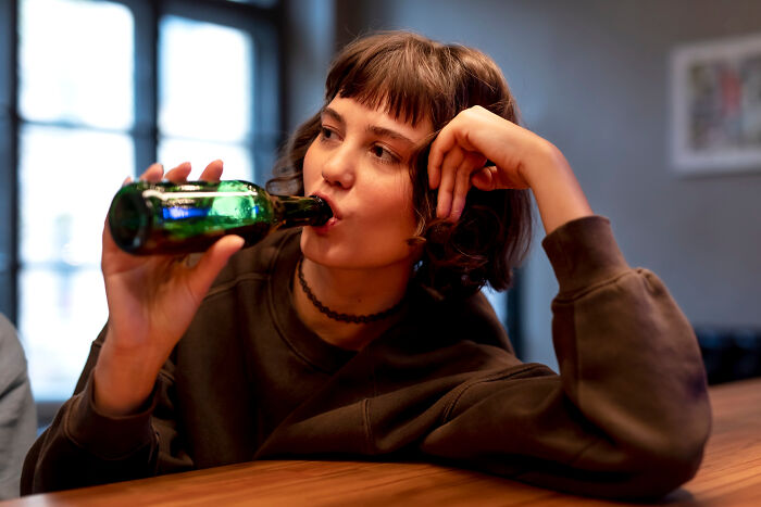 Young woman in casual wear drinking from a green bottle, reflecting on life-changing sentences tattooed on hearts.