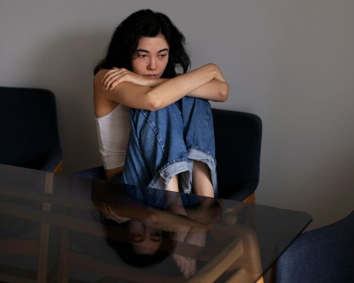 Young woman sitting alone at a glass table, looking thoughtful and sad, reflecting the moment of falling out of love.