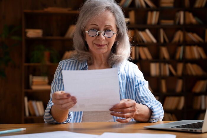 Middle-aged woman reading estate documents at home, showing reaction to inheritance split between hubby and niece.