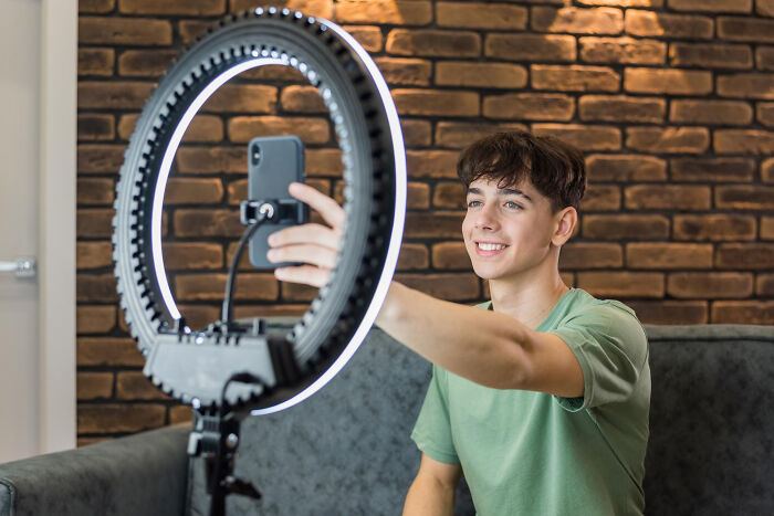 Teen boy smiling and taking a selfie with a smartphone and ring light, illustrating absurd dealbreakers in relationships.