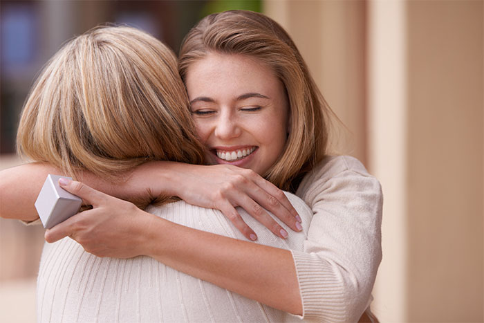 Teen girl smiling and hugging woman, contrasting with the theme of disappointment and hurt from parents gift.
