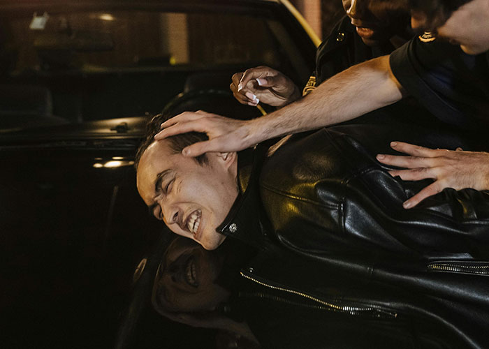 Man in a leather jacket being arrested by police officers in a nighttime scene of criminal fails.