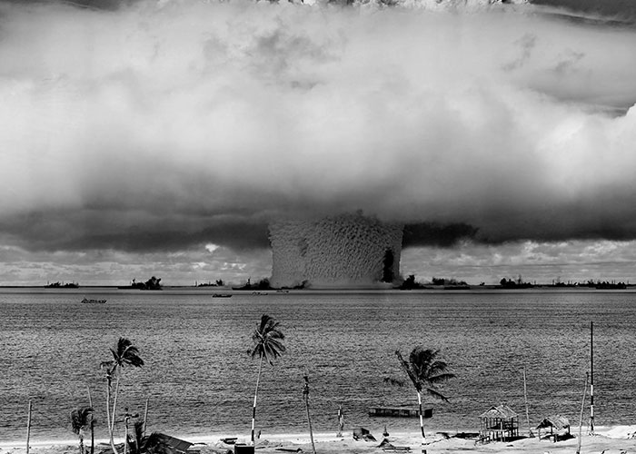 Mushroom cloud from a massive explosion over the ocean near a palm tree-lined beach in a terrifying true story.