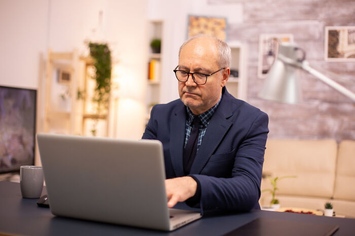 Older man in glasses and suit working on laptop, representing shocking school incidents involving a principal and secret affairs.