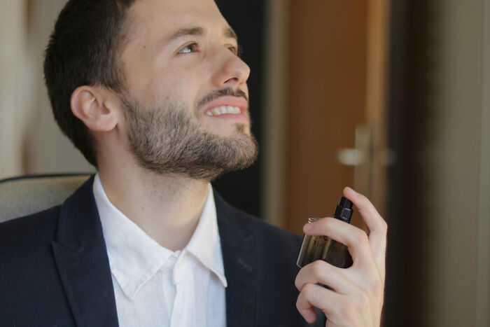 Man in a blazer applying cologne, illustrating one of the most absurd dealbreakers in relationships revealed by women.