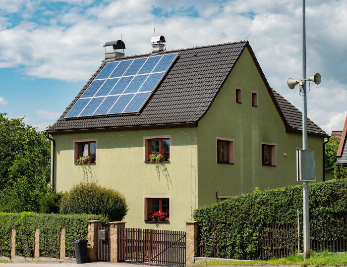 Green house with solar panels on roof under blue sky, illustrating mind-boggling adult conversations and survival questions.