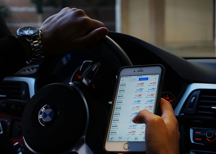 Person holding phone while steering BMW car, illustrating distracted behavior linked to criminal fails moments.