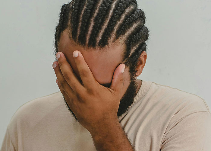 Man with braided hair covering his face in frustration, symbolizing hidden gems people discovered after moving into new homes.