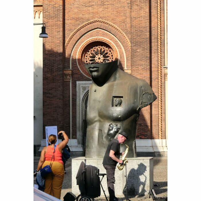 Street photo of a saxophone player creating a funny coincidence with a sculpture in an urban outdoor setting.