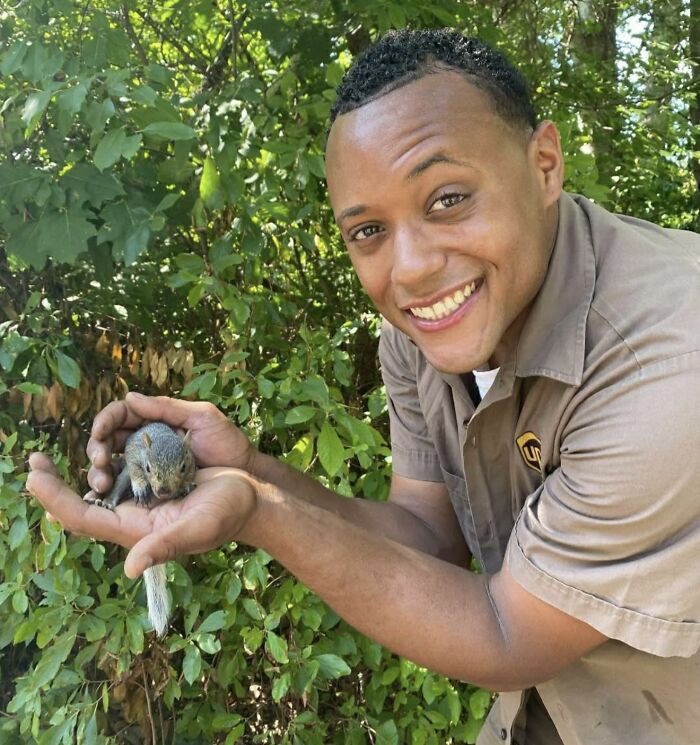 UPS driver smiling while holding an adorable squirrel outdoors surrounded by green foliage in a heartwarming moment with pets.