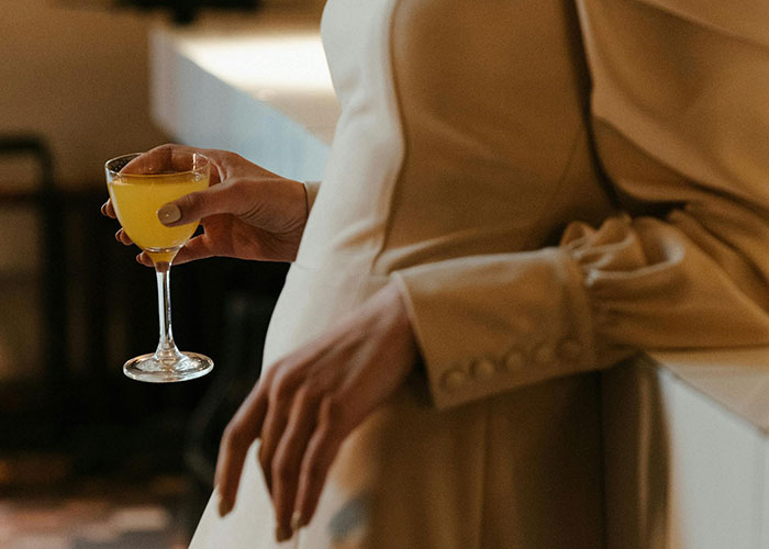 A person in a beige outfit holding a cocktail glass, capturing a moment of subtle body language and atmosphere.