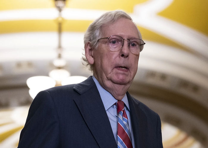 Older man in suit and glasses speaking indoors, representing historical events with significant damage to society.