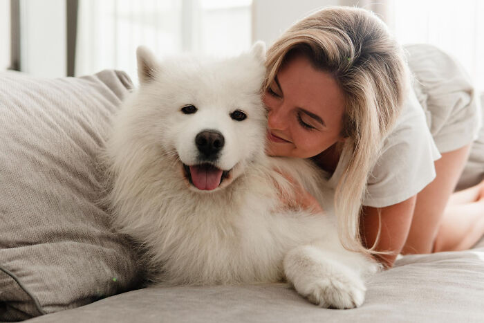 Woman cuddling a happy fluffy dog on a couch, illustrating comforting moments amid shocking family secrets revealed.