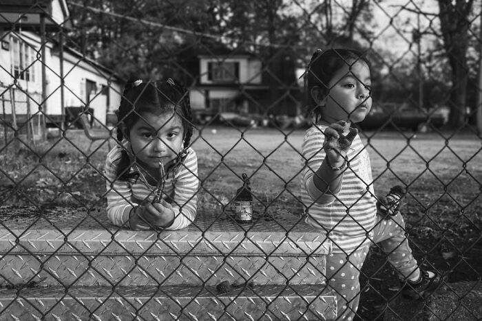 Two children behind a chain-link fence in a black and white powerful photograph of children of the world.