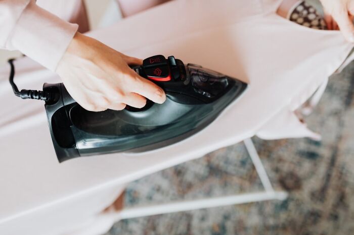 Person ironing light-colored pants on ironing board, demonstrating everyday adulting skills at home.