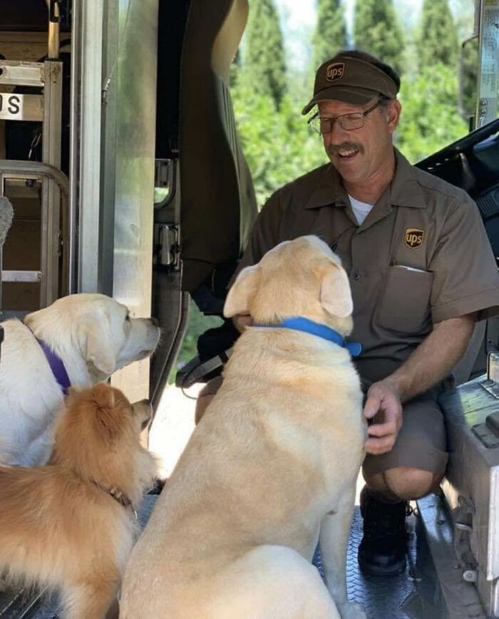 UPS driver smiling and interacting with three adorable pets inside a delivery truck during a break.